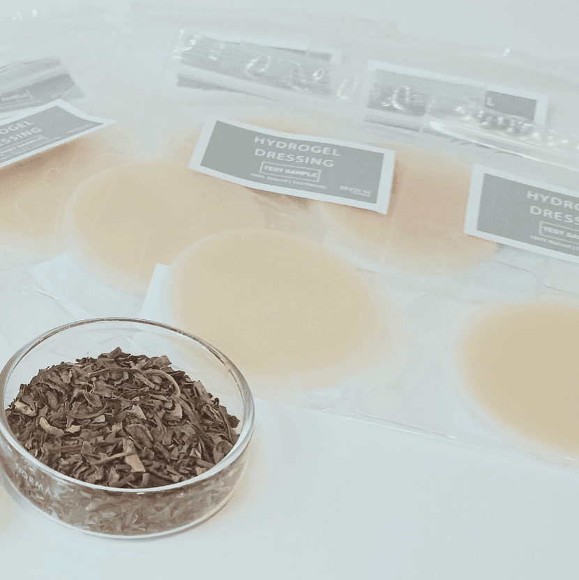 Curativos de hidrogel circulares em embalagens plásticas ao lado de uma tigela com ervas secas.